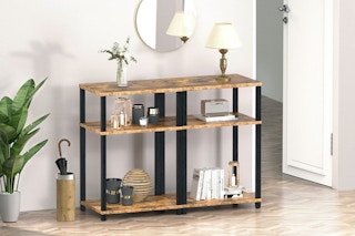 Two 3-tier end tables are pushed together to make one console table, which stands in a hallway between a plant and a door.