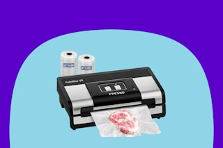 A black and silver deluxe-looking vacuum sealer is sealing some raw meat. Behind it are two bag rolls.