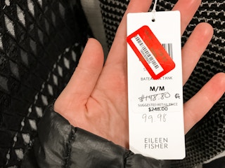 A person holding a price tag with a lower price hand written on it then what is visible on the red price tag. 