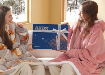 two women wearing heated blankets on a couch