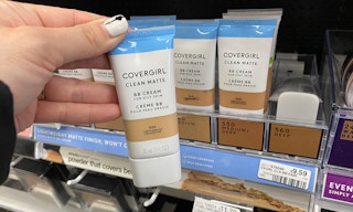 A hand holding Covergirl BB Cream in a store aisle.