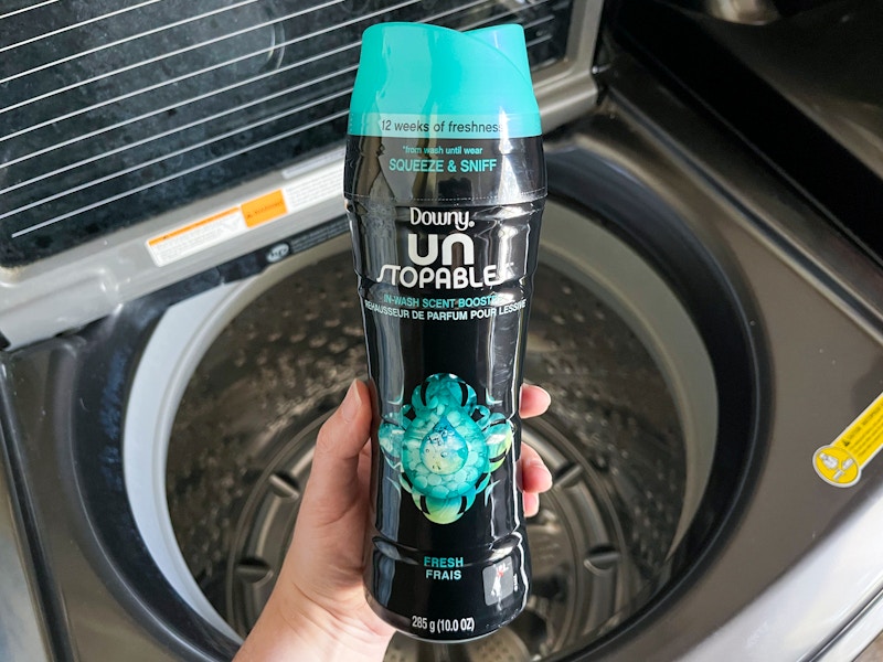 A person's hand holding a bottle of Downy Un Stopables laundry scent boost over an open washing machine.