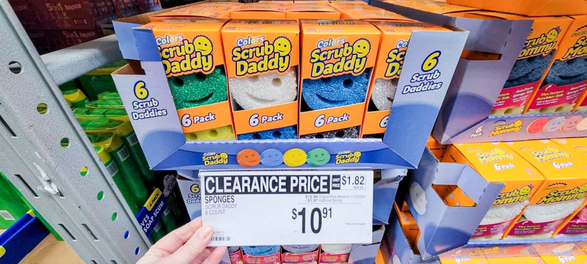 person holding a clearance sign for $10.91 scrub daddy sponges in front of the sponge display