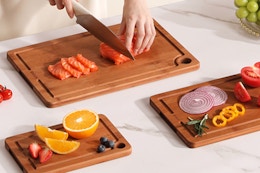 cutting boards B0FHW3MNKN Three bamboo cutting boards on a marble countertop with veggies and fruits on them