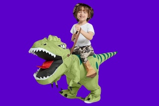 A child wears a costume that makes it look like he's riding a dinosaur on a purple background.