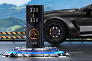 A tire inflator - air compressor is center frame. Behind it is a large black vehicle and some hills.