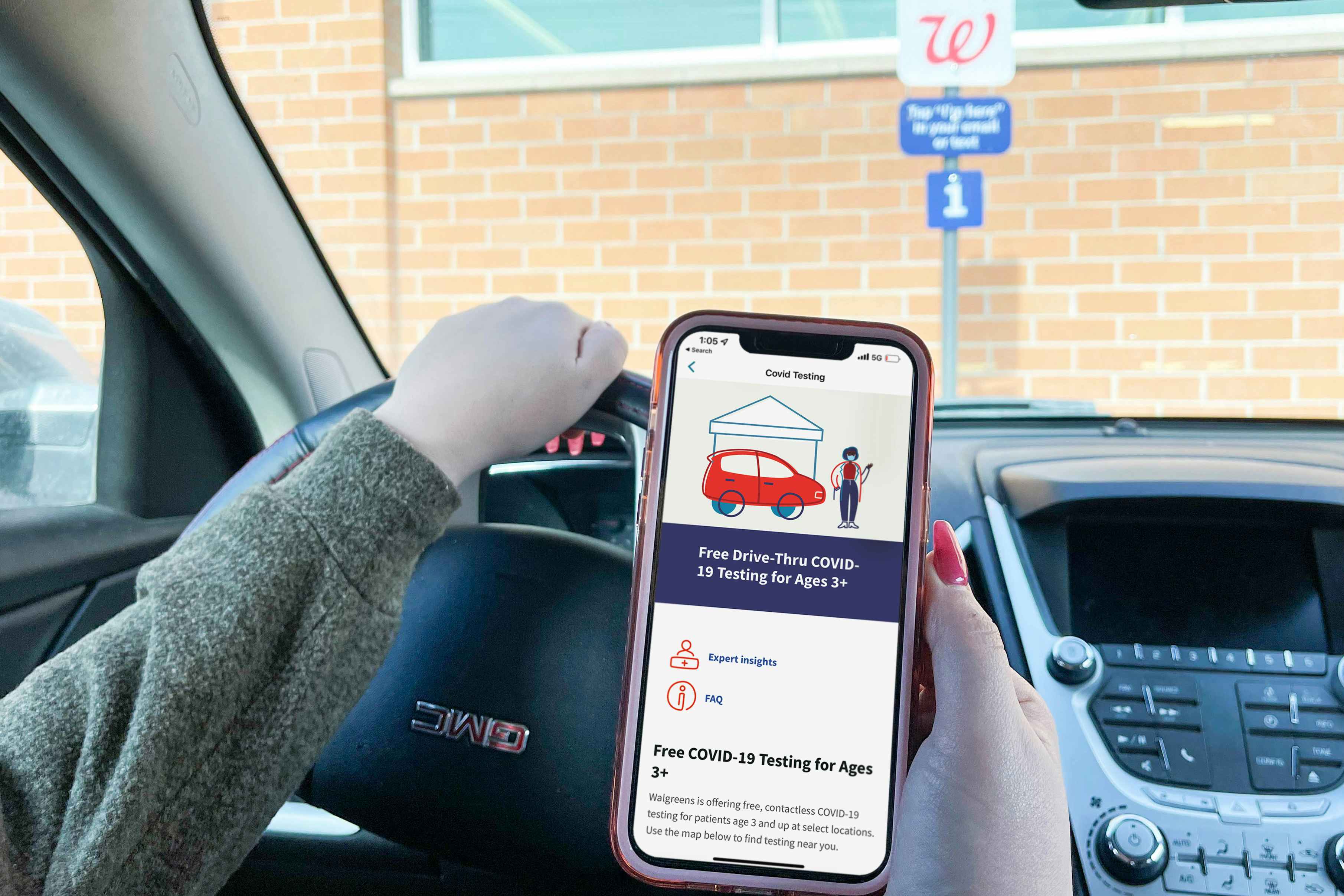 A person sitting in their car, parked in a Walgreens parking lot and holding their phone displaying the drive thru COVID-19 testing infor...