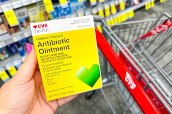 person holding cvs health antibiotic ointment over a cvs cart