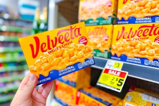 hand holding velveeta shells and cheese in front of dollar general shelf