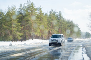 cars drive on a slick, muddy and snowy road with all weather tires
