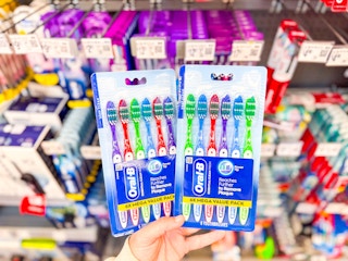 hand holding two 6-packs of Oral-B toothbrushes