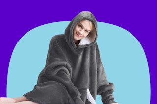 A woman sits in front of a blue background with a purple arch wearing a plush grey sherpa-lined hoodie.