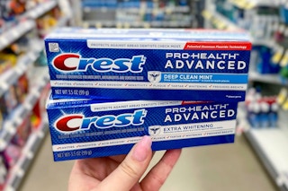 hand holding two tubes of crest toothpaste in a store aisle