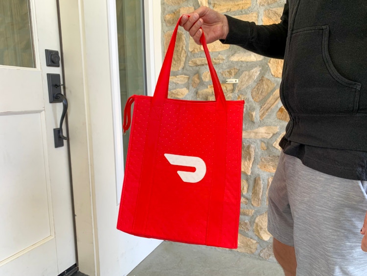 A man delivering food in a doordash bag.