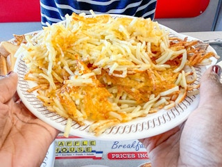 A person's hands holding up a plate of hash browns at a table at Waffle House.