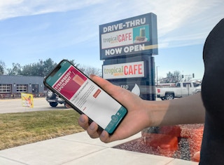 Tropical Smoothie Cafe app in hand with coupons displayed, store sign in the background