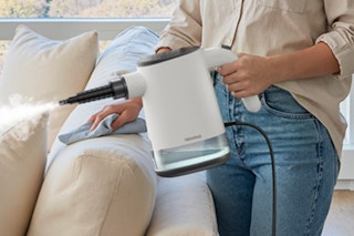 Woman using the TEEVOGO Steam Cleaner on her couch.