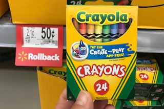 A person's hand holding a box of 24 count Crayola crayons next to a Walmart rollback price tag for $0.50