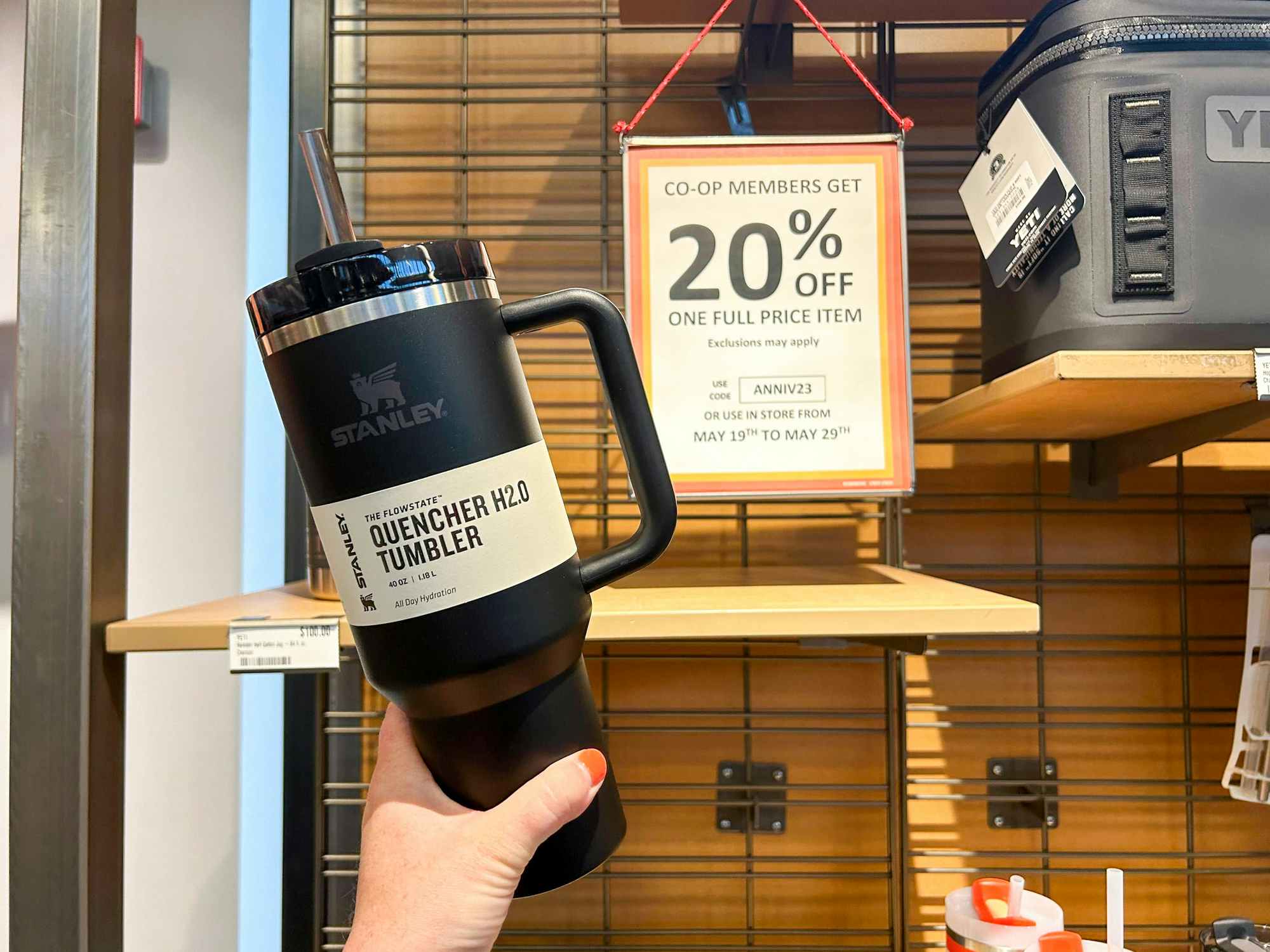 Someone holding a Stanley tumbler in front of a 20% off sign in REI