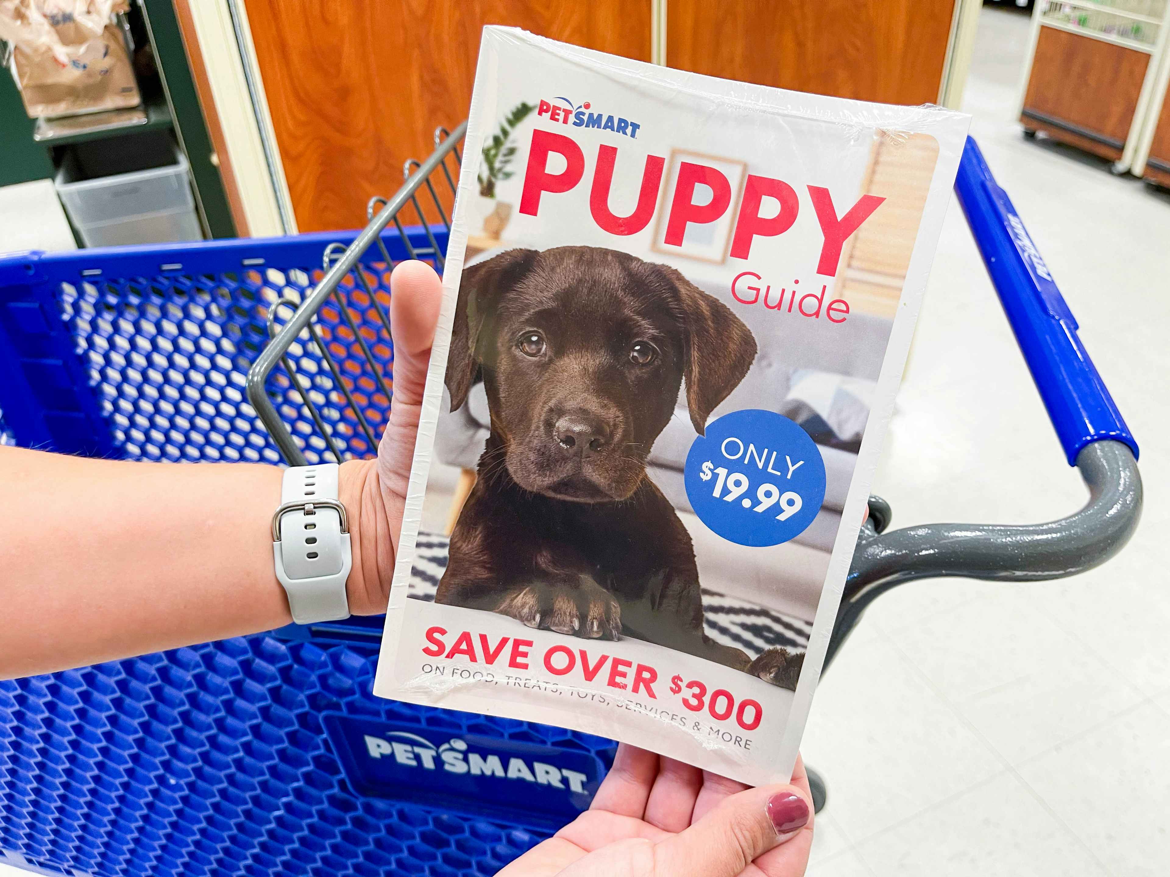 A person's hands holding up a PetSmart Puppy Guide in front of a PetSmart shopping cart.