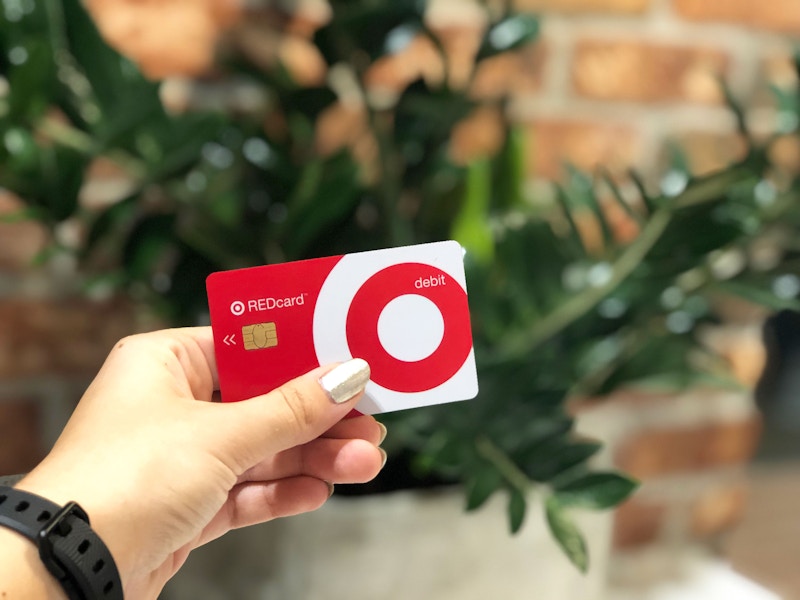 A person's hand holding up a Target RedCard in front of a plant.