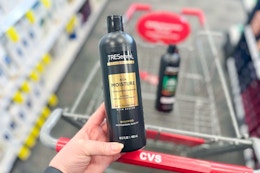 person holding a bottle of tresemme shampoo over a cvs cart