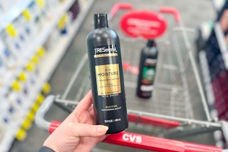 person holding a bottle of tresemme shampoo over a cvs cart
