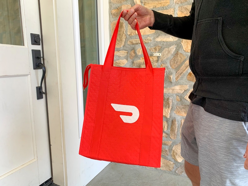 A man standing on a front porch, delivering food in a doordash bag.