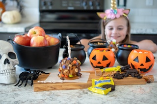 Caramel apple, apples, and candy in a small plastic cauldrons and pumpkins.