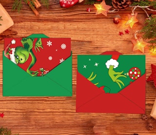 Grinch-themed Christmas cards in envelopes on a wooden table