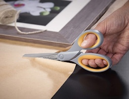 a hand with scissors cutting a piece of brown paper