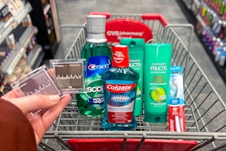 A person's hand holding up two Maybelline eyeshadows in front of a CVS shopping cart with Colgate and Garnier Fructis products in the ...