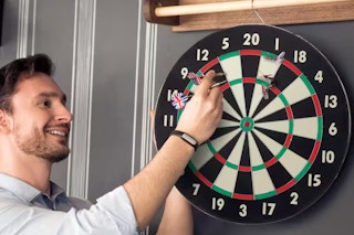 lifestyle image of a man taking darts off a dart board