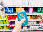 a hand holding a bottle of shampoo in a store aisle