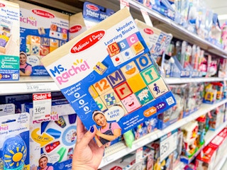 hand holding a miss rachel x melissa & doug block set in front of toys