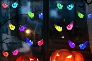 Several pairs of Halloween eyes glow in a window above glowing pumpkins.
