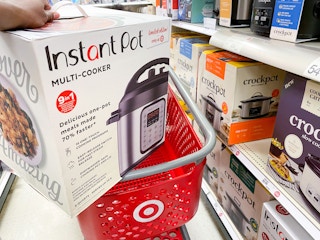 A person putting an Instant Pot 6-Quart 9-in-1 Bundle in its box into a Target shopping cart.