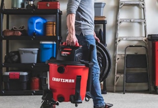 a guy carrying a wet/dry vacuum in a garage