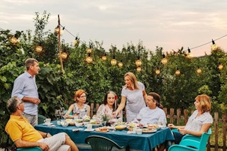 a group of people sitting outside at a table with string lights and trees in the background