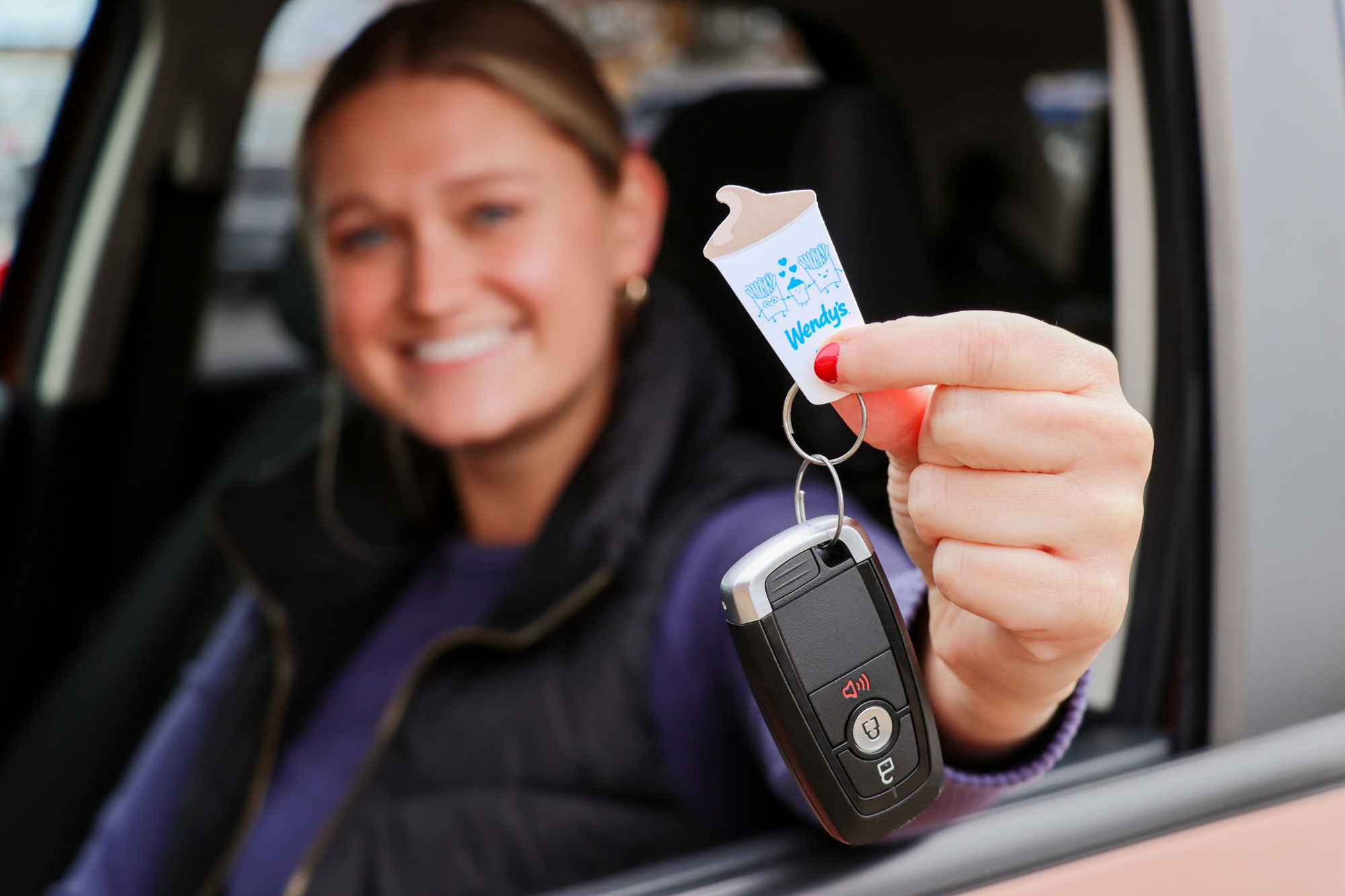 a person holding out a frosty key tag while sitting in a car