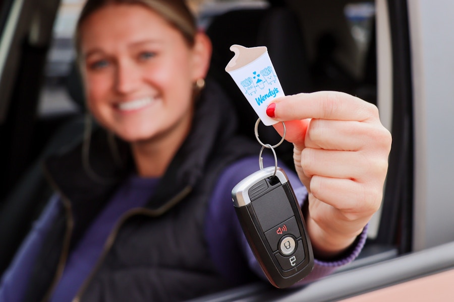 a person holding out a frosty key tag while sitting in a car