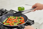 tongs tossing vegetables in pan