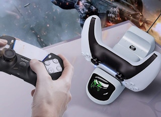 A person playing a game on a PS5 controller, next to another PS5 controller charging on a dock.