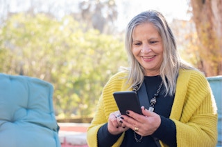 An older woman in a yellow shawl woman smiles while using her phone
