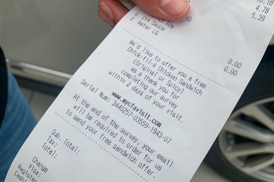 A person's hand holding a Chick-fil-A receipt showing an offer of a free chicken sandwich for completing the survey.