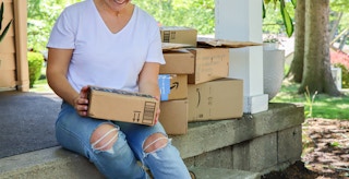 a person smiling while sitting on a front porch with amazon boxes