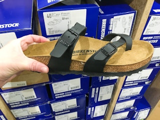 A person's hand holding a Birkenstock sandal in front of Birkenstock shoeboxes.