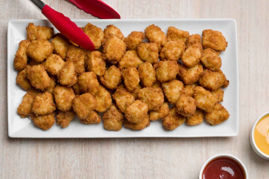 A large platter of Chick-fil-A chicken nuggets on a table next to some tongs and dipping sauces.