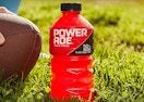 a bottle of red Powerade in grass next to a football