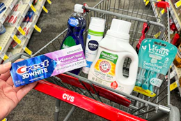 person holding crest toothpaste over a cart with palmolive dish soap, nivea shave gel, arm & hammer detergent, and venus razors in it
